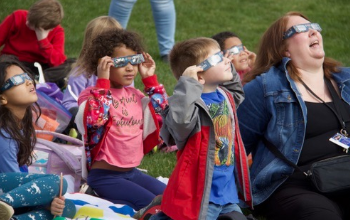 children and teacher with eclipse glasses on look up at the sky