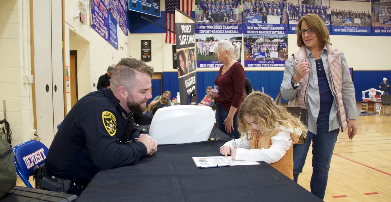 little girl signs paper while sheriff deputy looks on