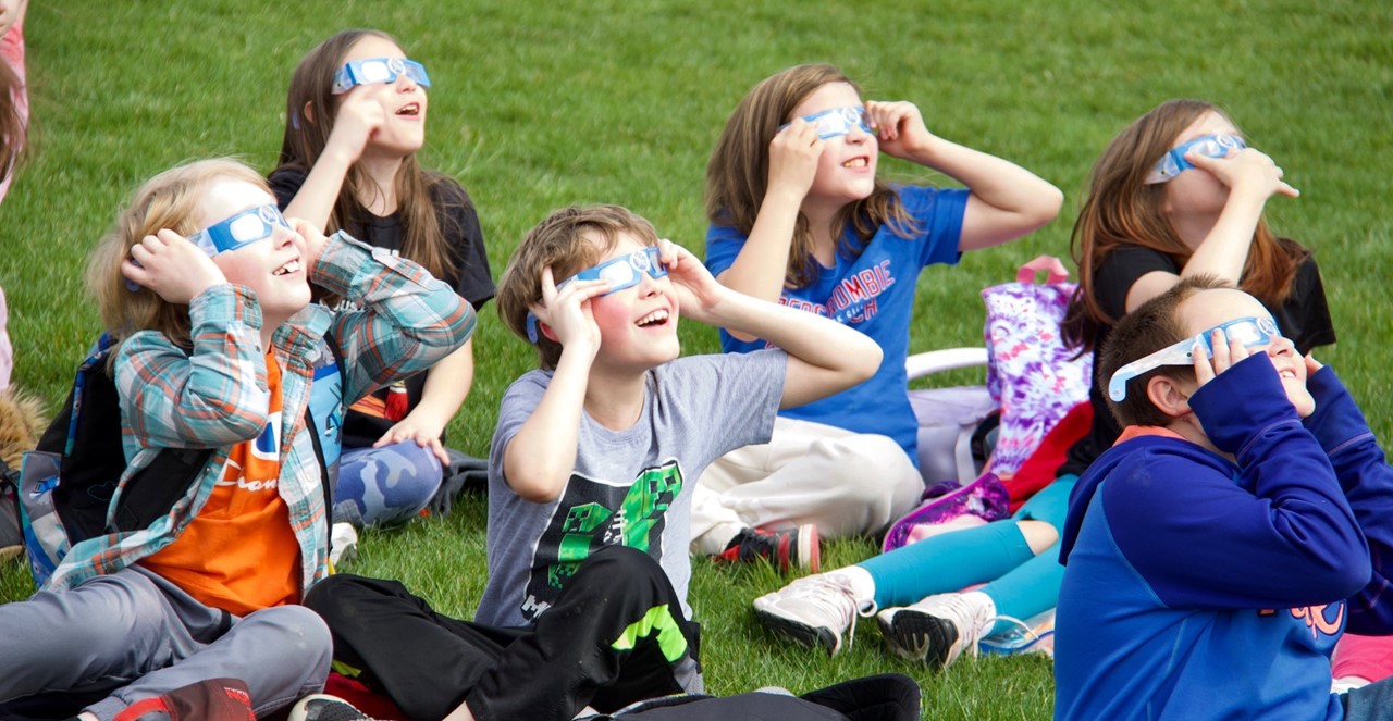 group of children with eclipse sunglasses on looking up at the sky